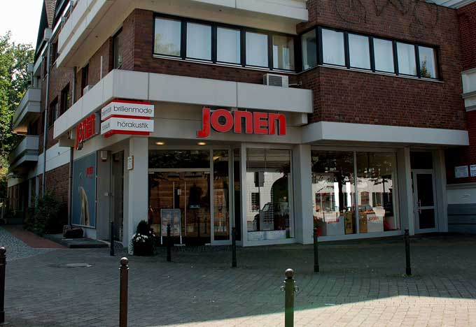 Optikerfachgeschäft mit rotem JONEN-Schriftzug und Schaufenstern in einem modernen Gebäude.
